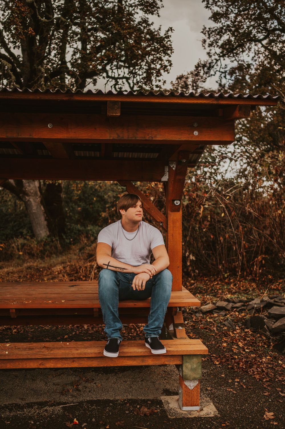 Person sitting alone on wooden bench during autumn with fallen leaves scattered around.