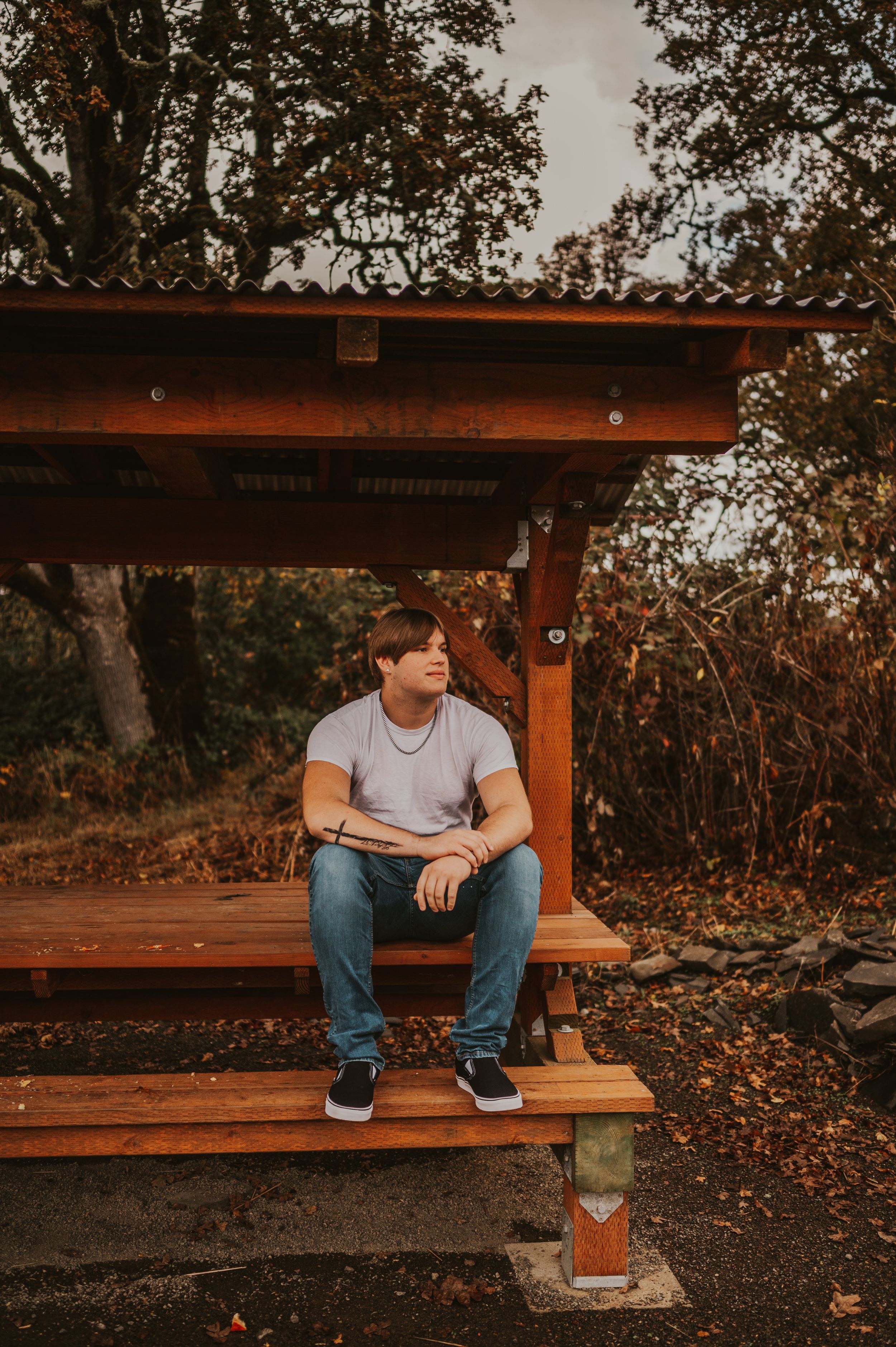 Person sitting alone on wooden bench during autumn with fallen leaves scattered around.