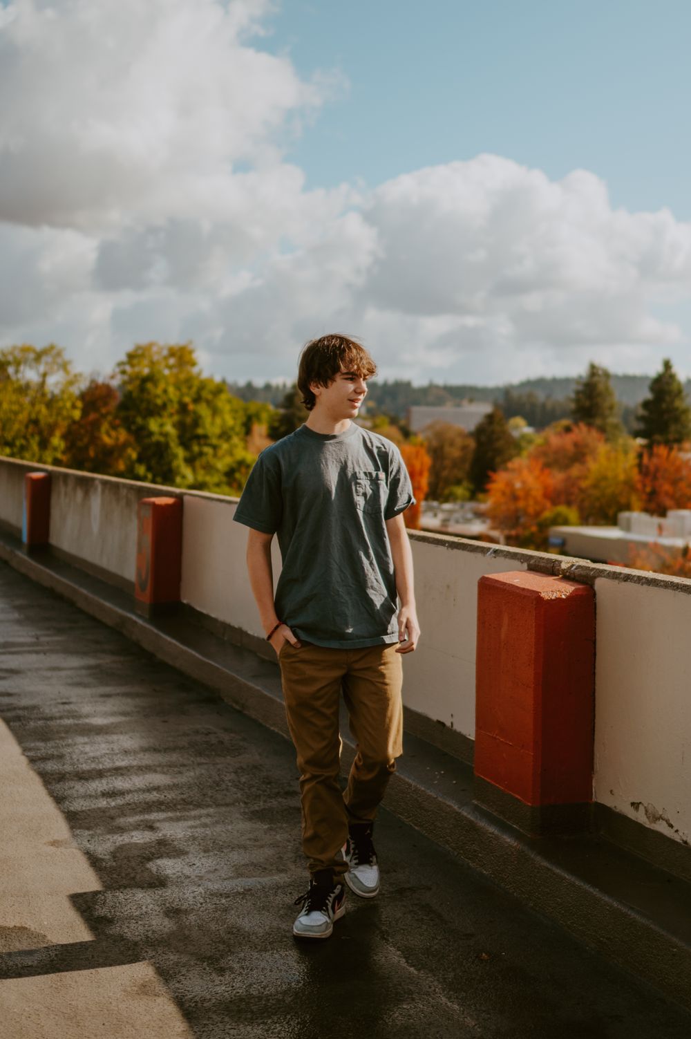 Person walking along rooftop pathway with autumn foliage and blue sky in background.