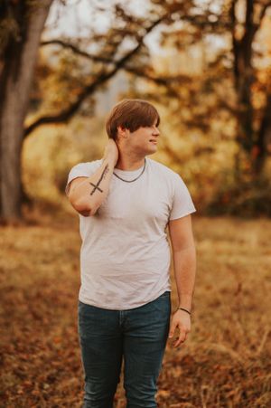 Person in casual attire poses against warm autumn background with fallen leaves.