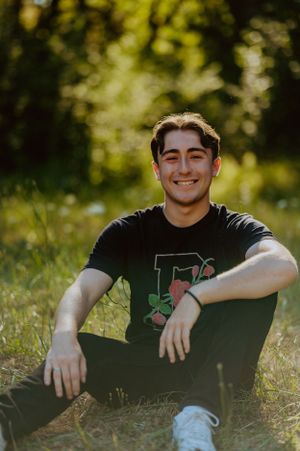 Young person in black t-shirt and white sneakers relaxing outdoors on grass.