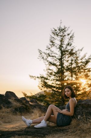 Person relaxing against rocky terrain during golden hour with pine trees in background.