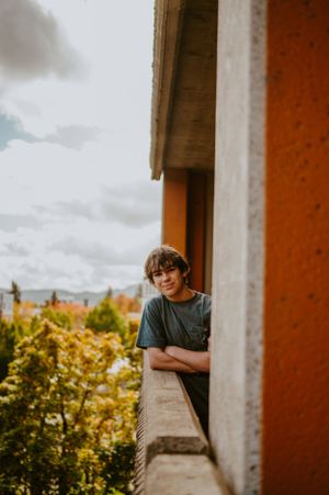 Person leaning against concrete structure with autumn trees visible in background.