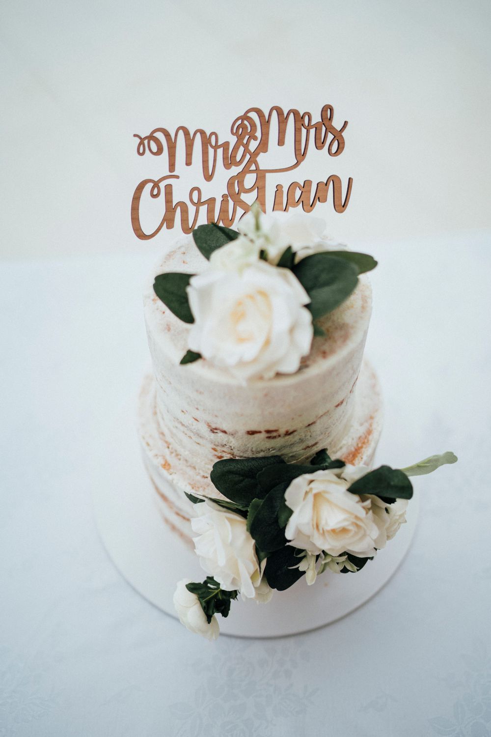 White two-tier wedding cake decorated with roses and a rose gold 'Mr & Mrs' topper.