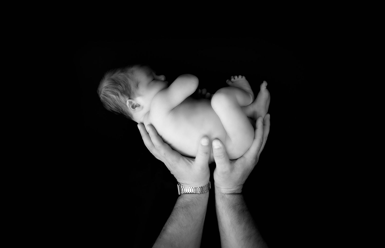 Black & White portrait, newborn shoot - baby being held up in hi daddy's hands