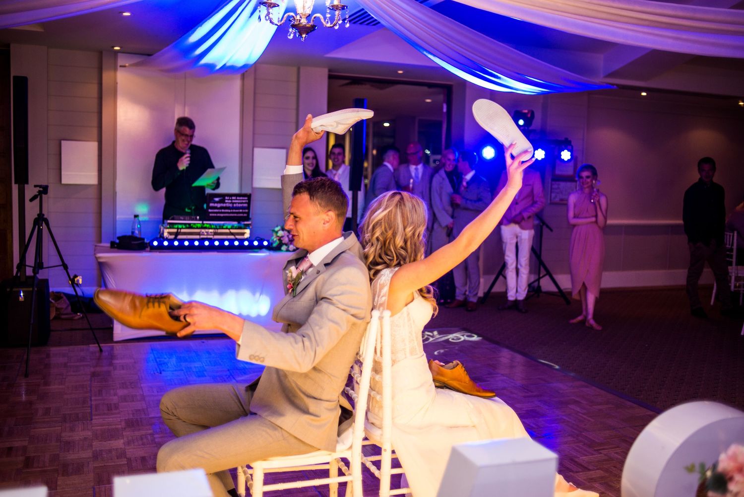 Wedding reception celebration with couple playing musical chairs game under blue lighting.
