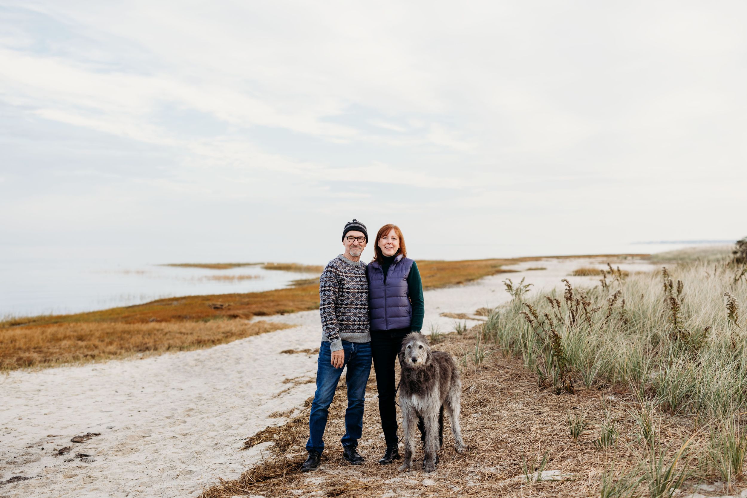 older couple walking dog in winter on beach