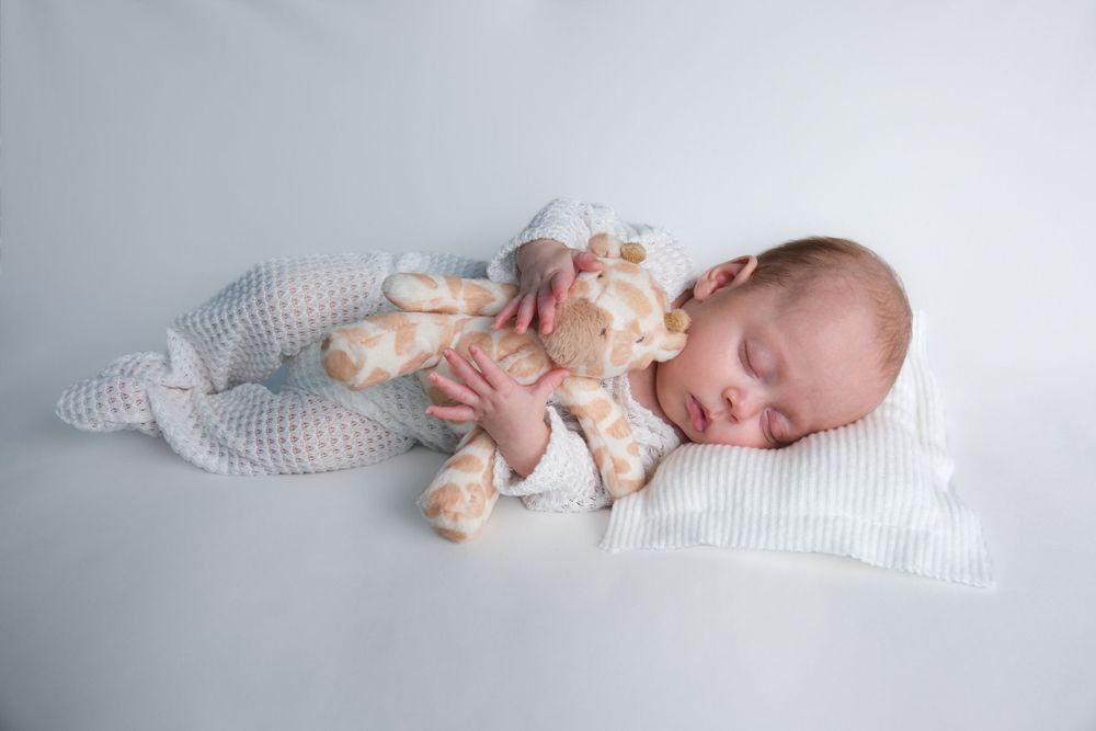newborn holding her mother's childhood teddy on side and pillow