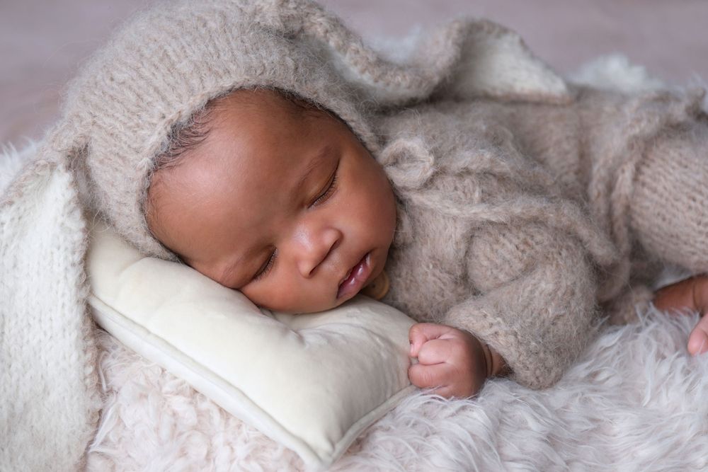Baby posed in wooden bowl prop wearing cute bunny ears during newborn photography session