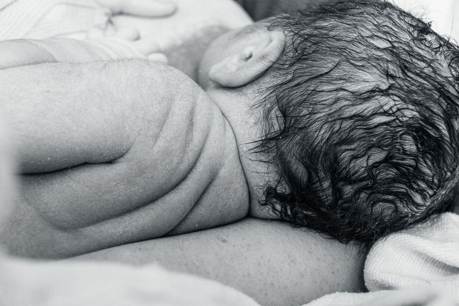 Black and white close-up of a newborn baby's head and shoulder resting on soft bedding.