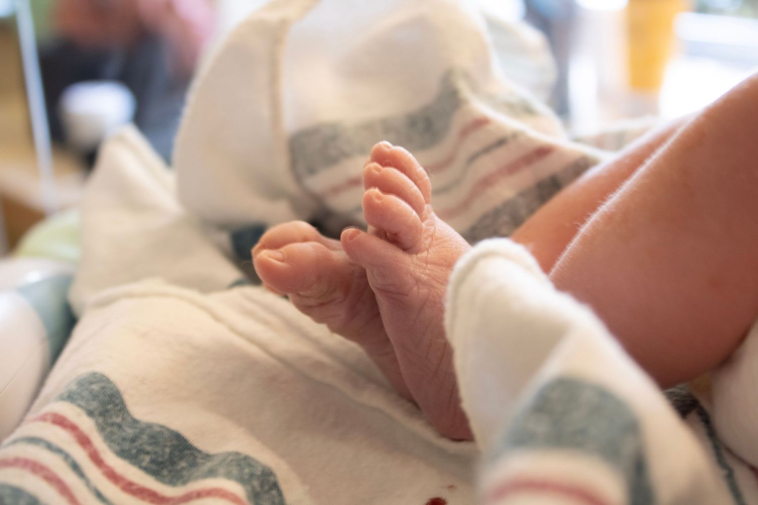 Close-up of tiny newborn baby feet wrapped in hospital striped blanket.