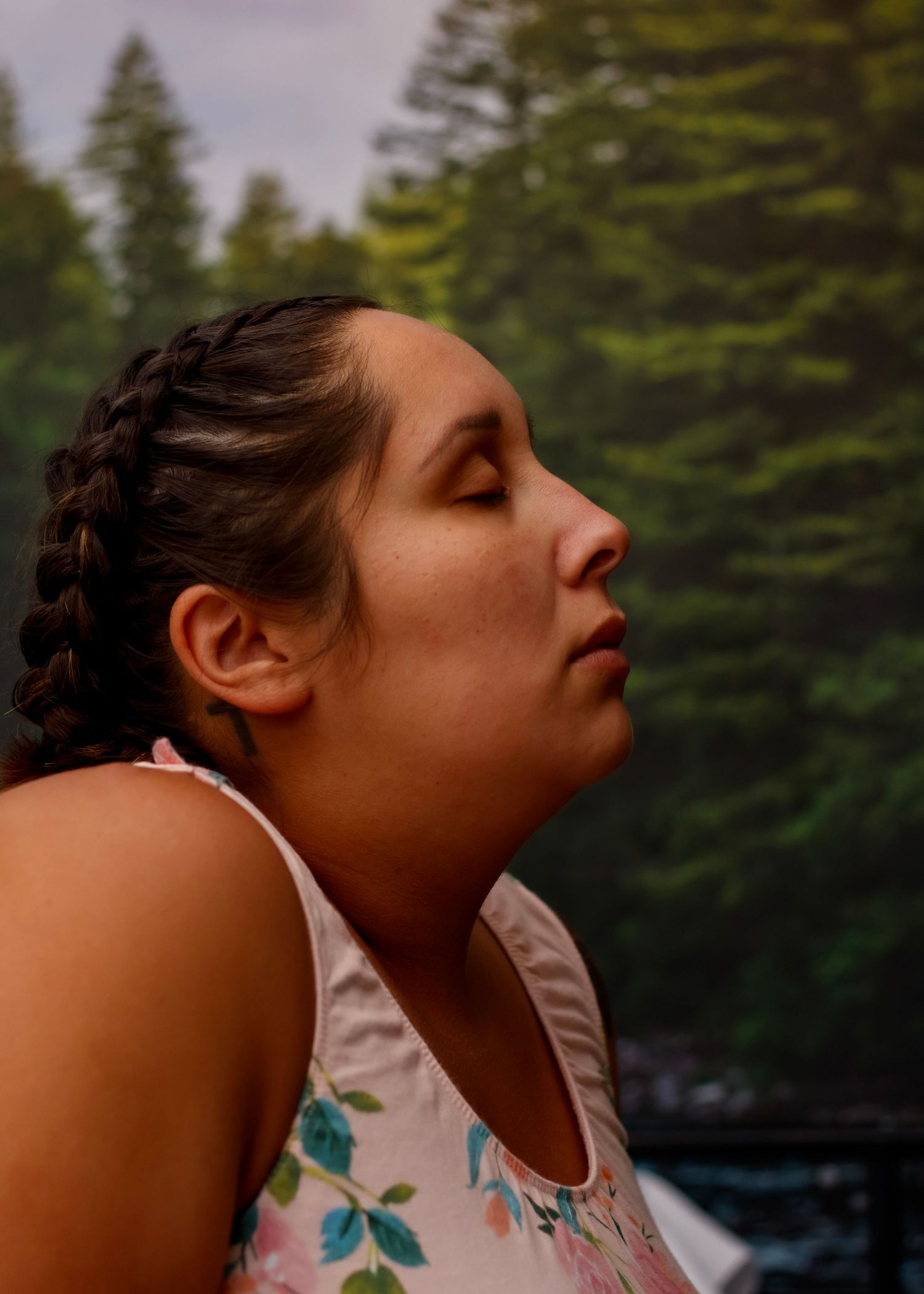 Person with braided hair meditating outdoors against forest backdrop.