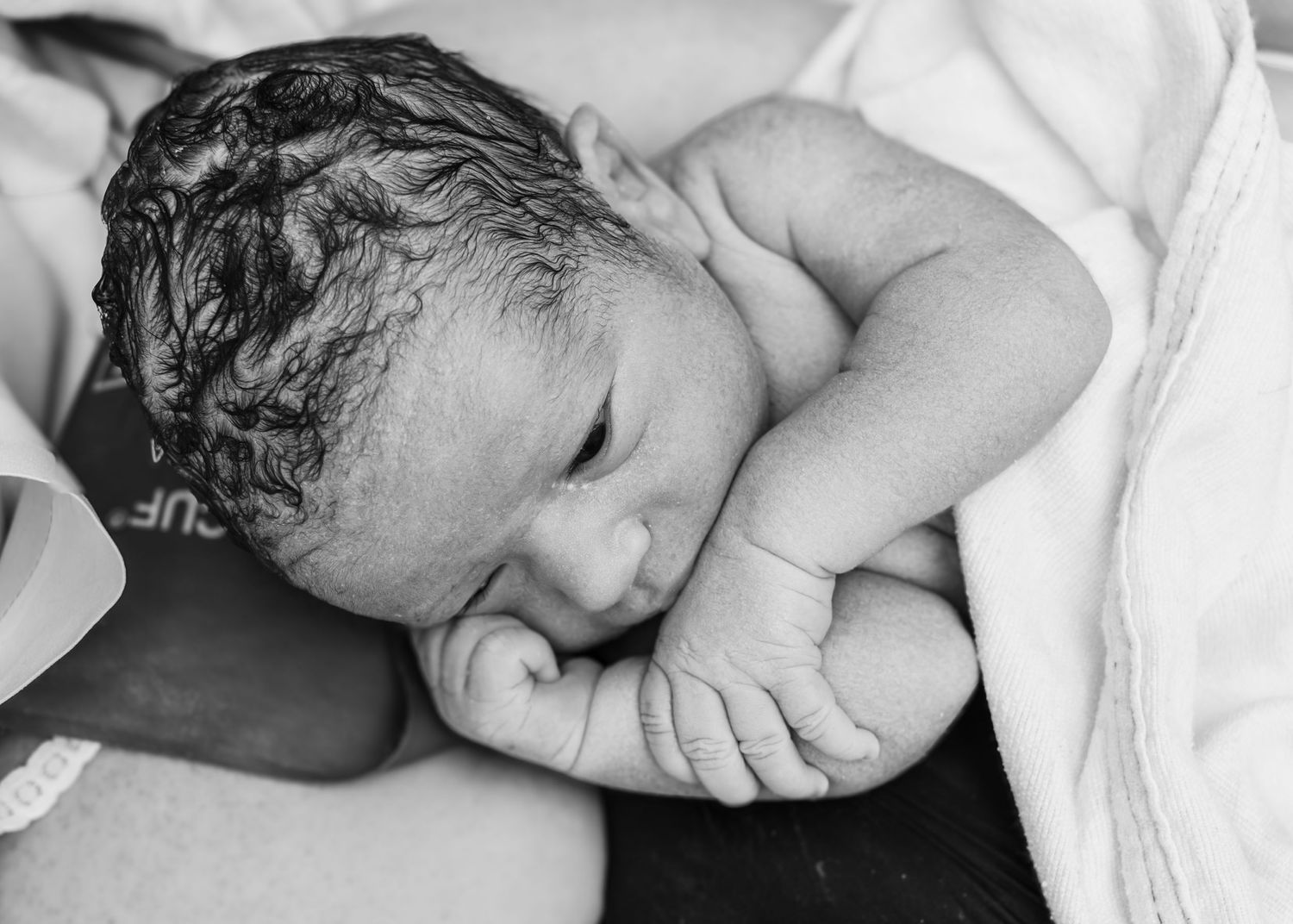 A newborn baby sleeps peacefully swaddled in white blankets in black and white photography.