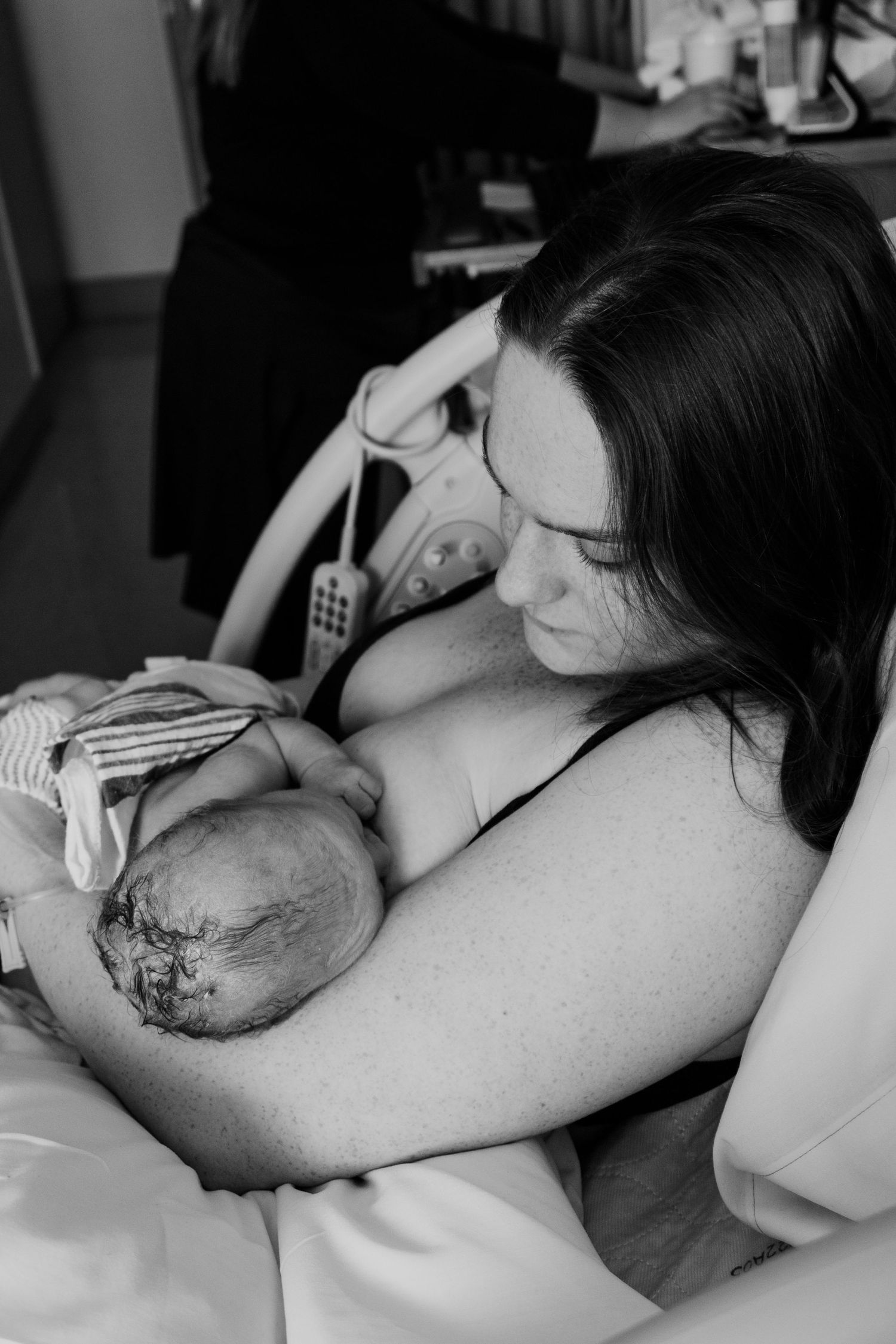 A newborn baby rests skin-to-skin on a parent's chest in a black and white hospital photo.