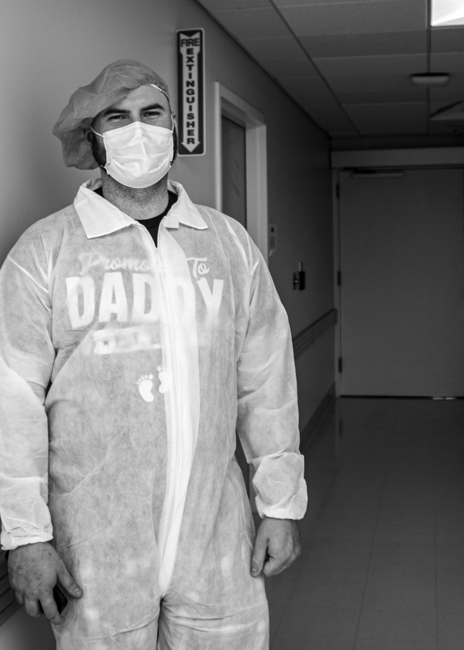 Healthcare worker wearing protective gear and face mask in hospital hallway showing daddy text on uniform.