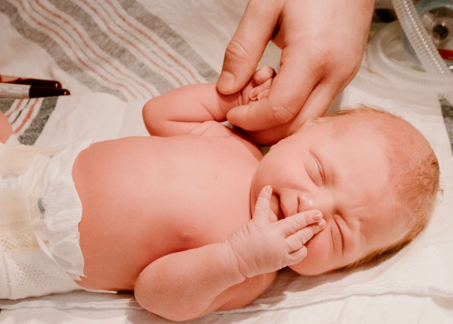 Newborn baby being examined with gentle touch during medical checkup.