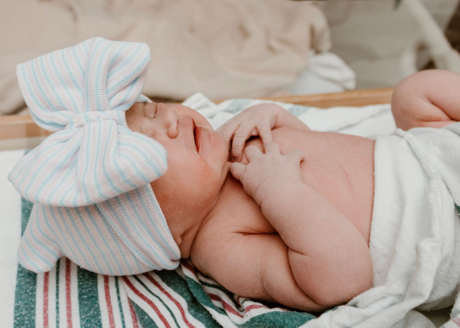 Newborn baby wearing white bow headband sleeping peacefully.