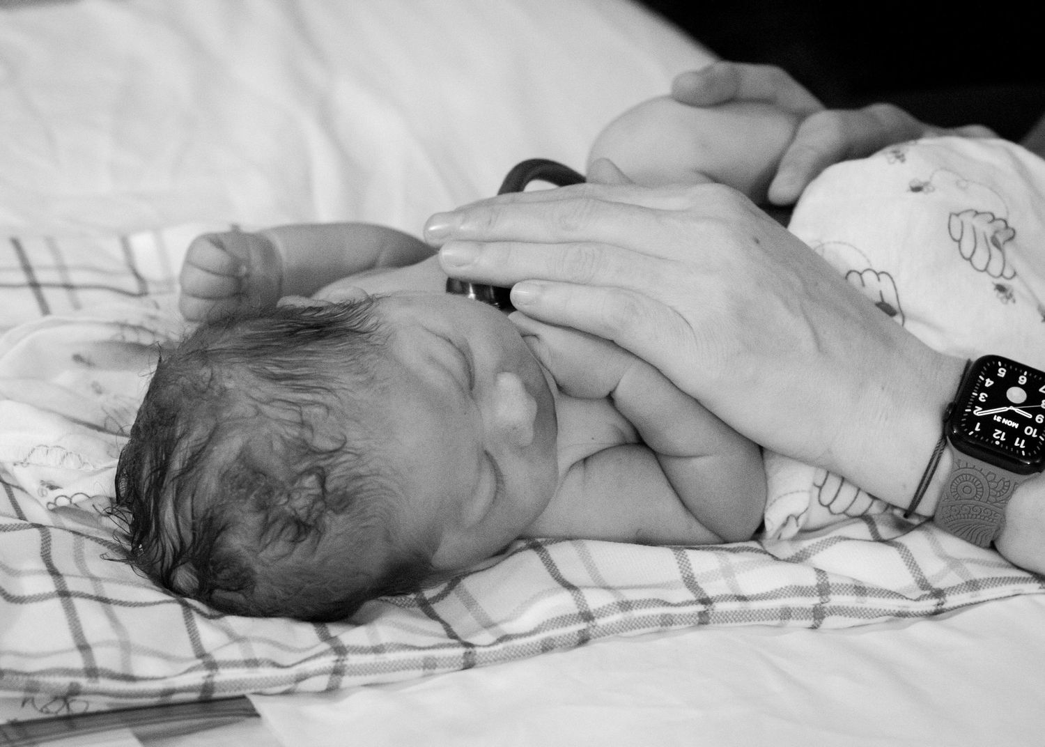 Newborn baby resting on hospital bedding while being gently touched.