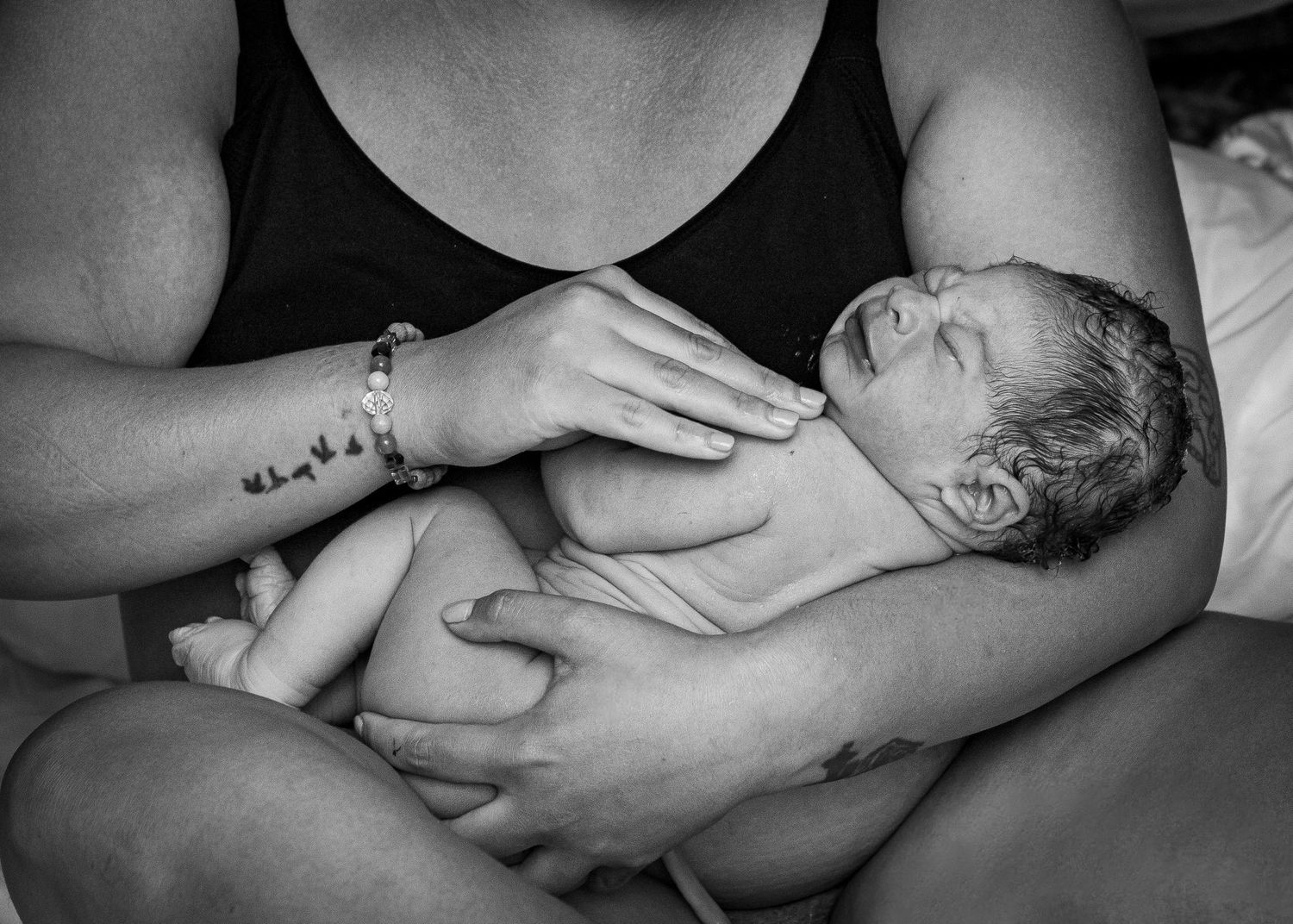 A tender moment showing hands cradling a newborn baby in black and white.