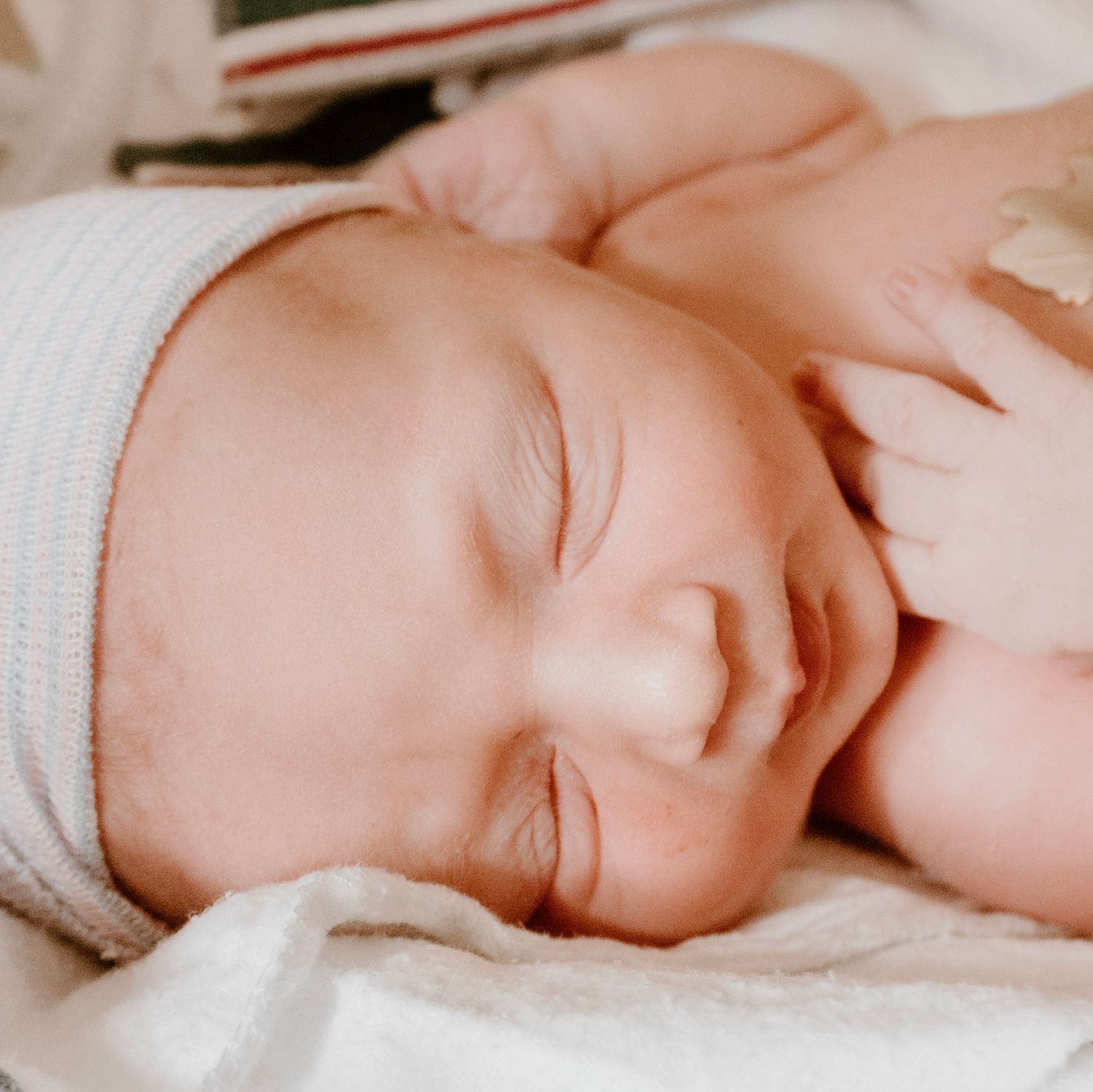 Peaceful sleeping newborn baby wearing white cap swaddled in blankets.