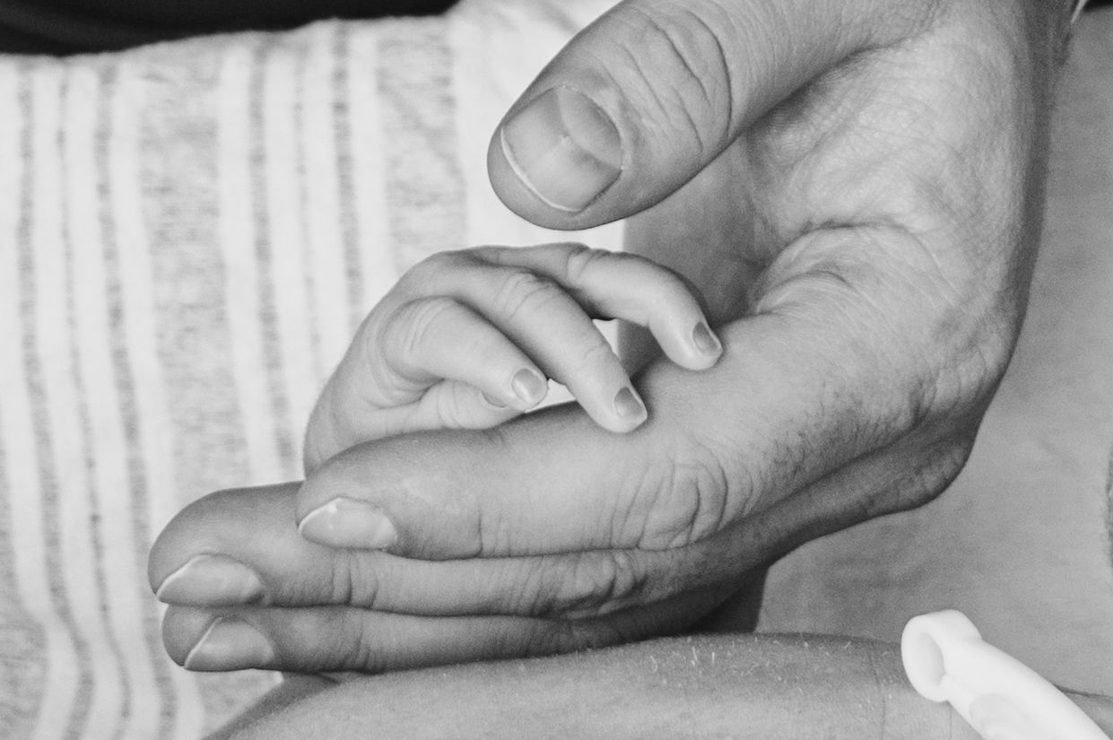 Black and white close-up of tiny baby fingers holding an adult's hand.
