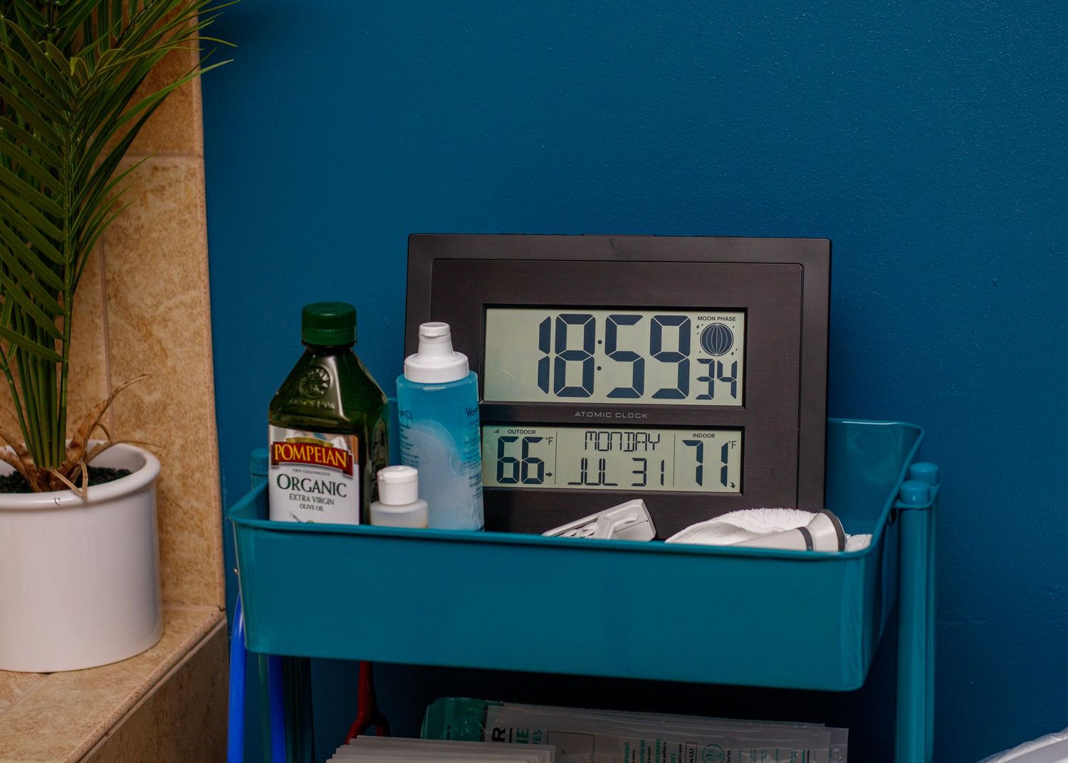 Digital clock and baby supplies arranged on blue shelf against teal wall.