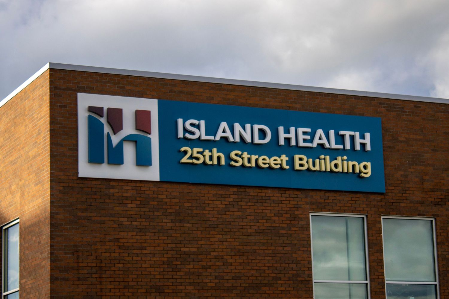 Island Health 25th Street Building exterior sign mounted on brick building under cloudy sky.