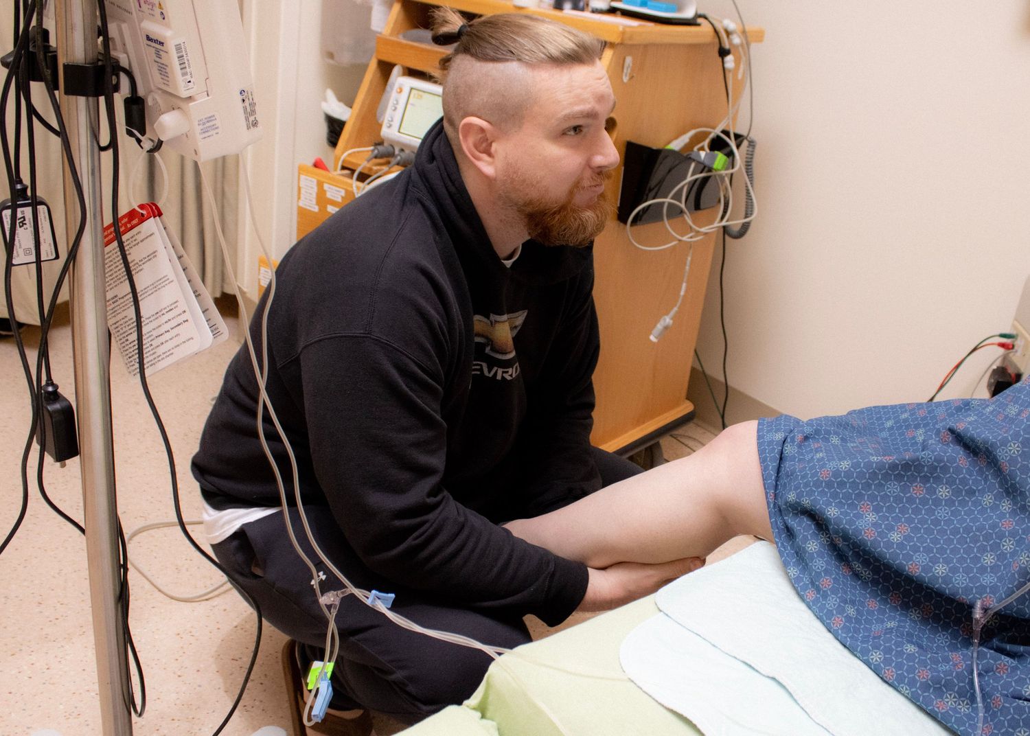 Medical professional in dark clothing attends to patient during hospital care.