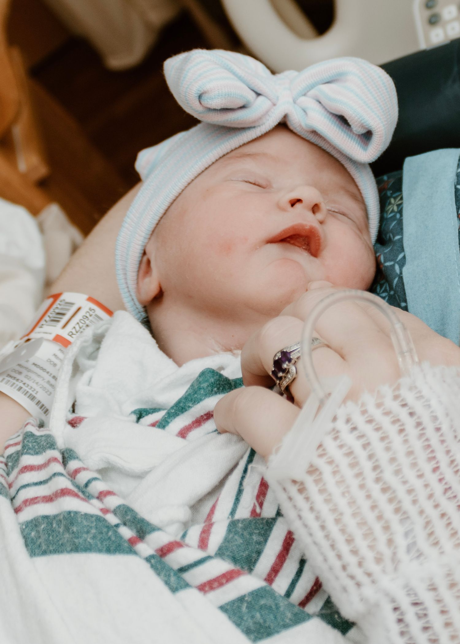 Peaceful newborn baby sleeping while wearing white bow headband and striped outfit.