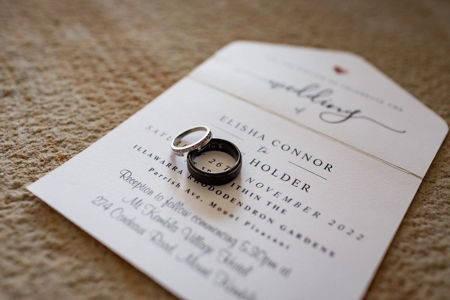 Wedding rings placed on an elegant white invitation card against a textured burlap background.