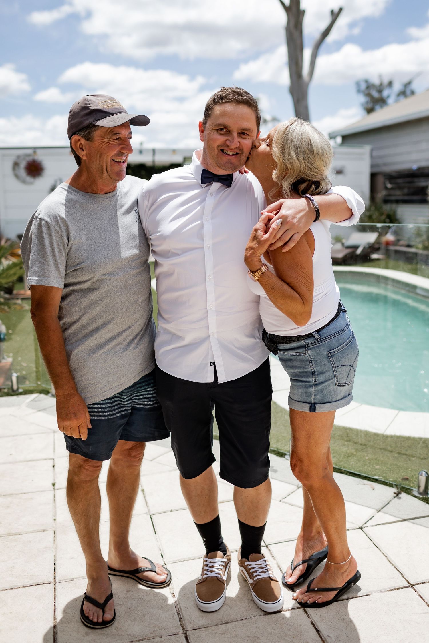 Three family members sharing a joyful moment by a swimming pool on a sunny day.