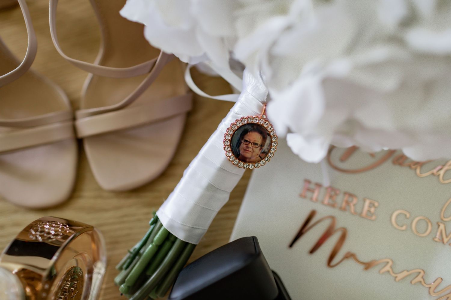 Wedding details including beige shoes, bouquet wrap, and personalized invitation on light surface.