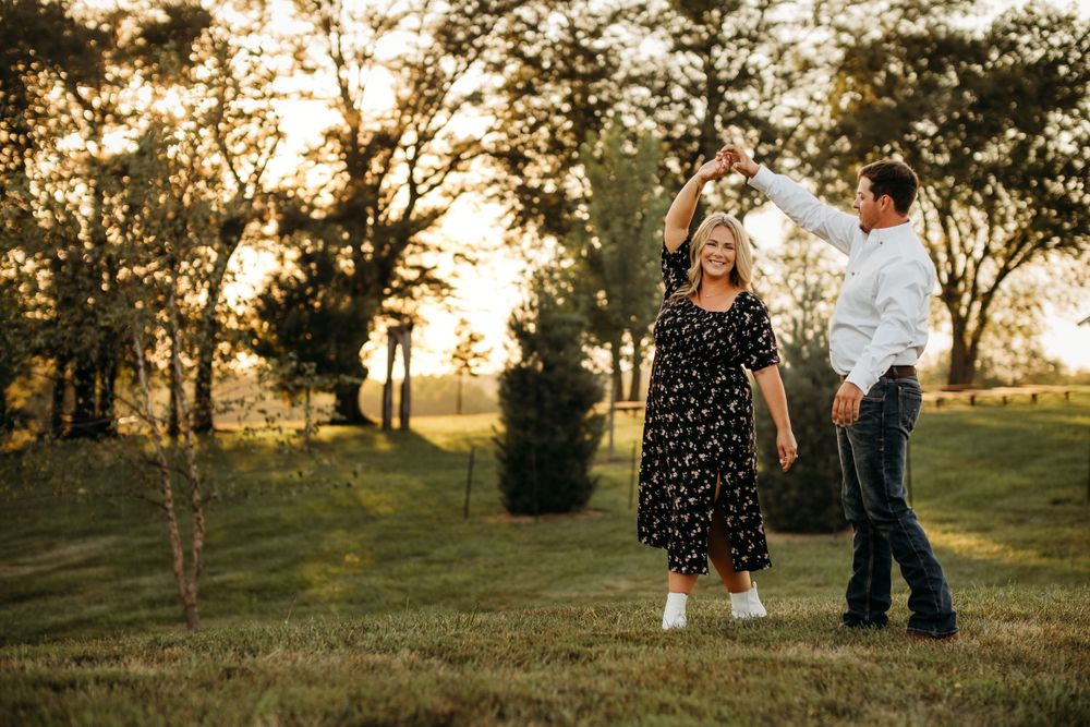 Woman in black dress smiles while dancing with a man in front of a field in Northwest Arkansas.