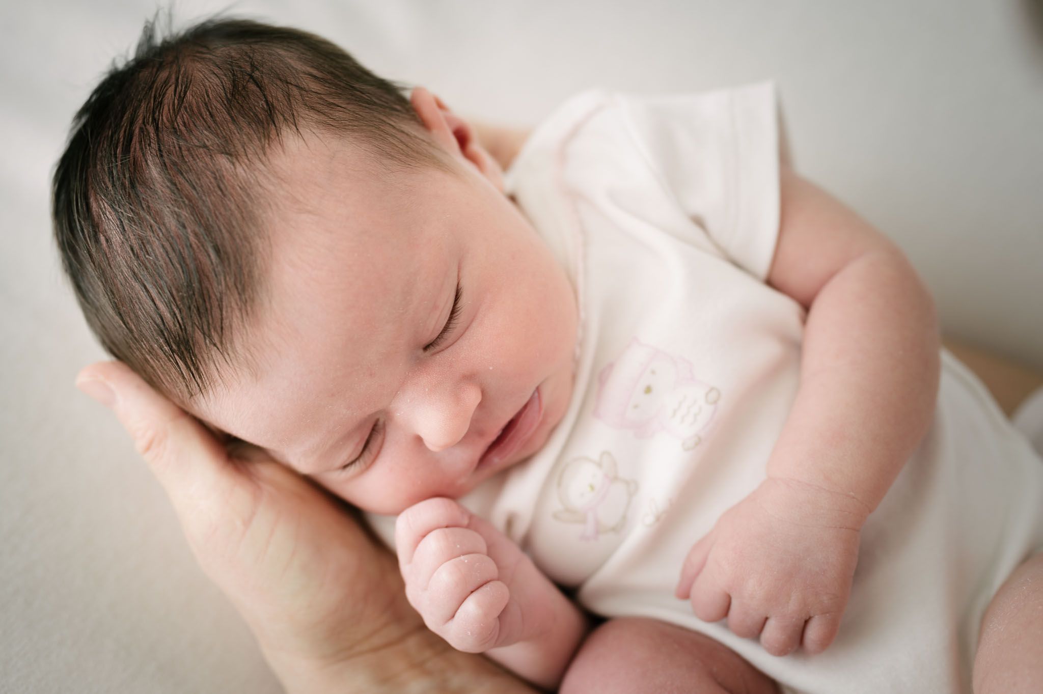 Peaceful sleeping newborn in white clothing nestled in caring hands.