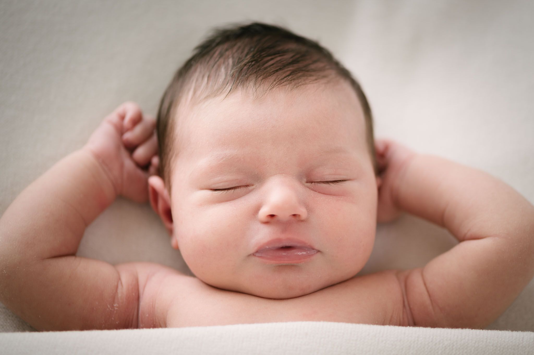 A peaceful sleeping newborn baby lying with hands behind head.