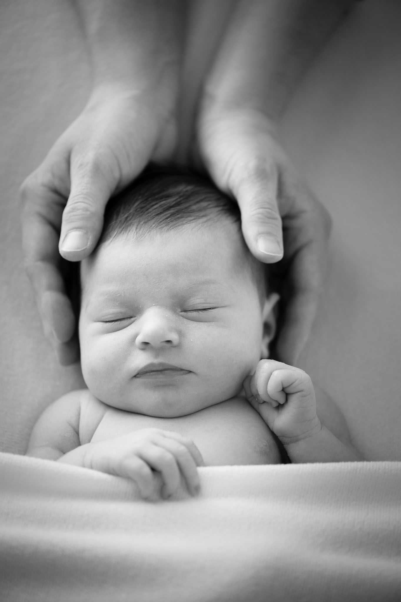 Gentle hands cradle a sleeping newborn against soft white fabric.
