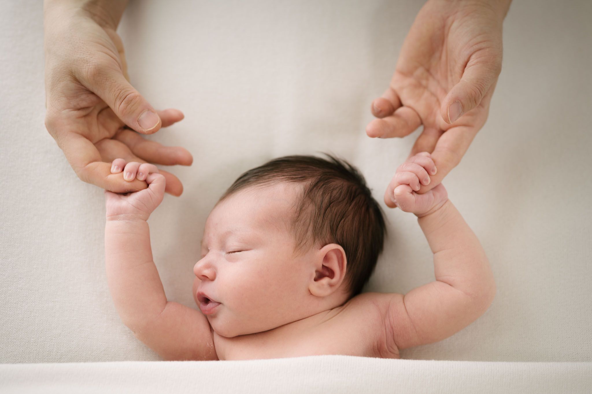 Tender moment of adult hands holding infant's arms during peaceful sleep.