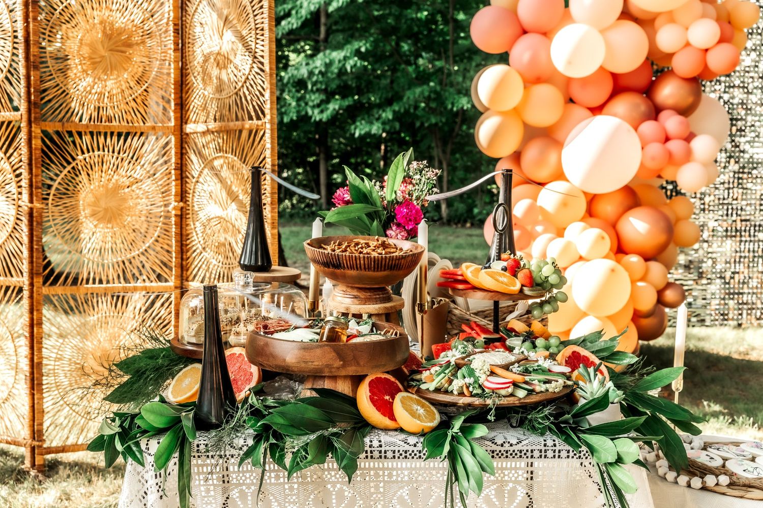 Festive party display with orange balloon arch, gold backdrop, and tiered food presentation.