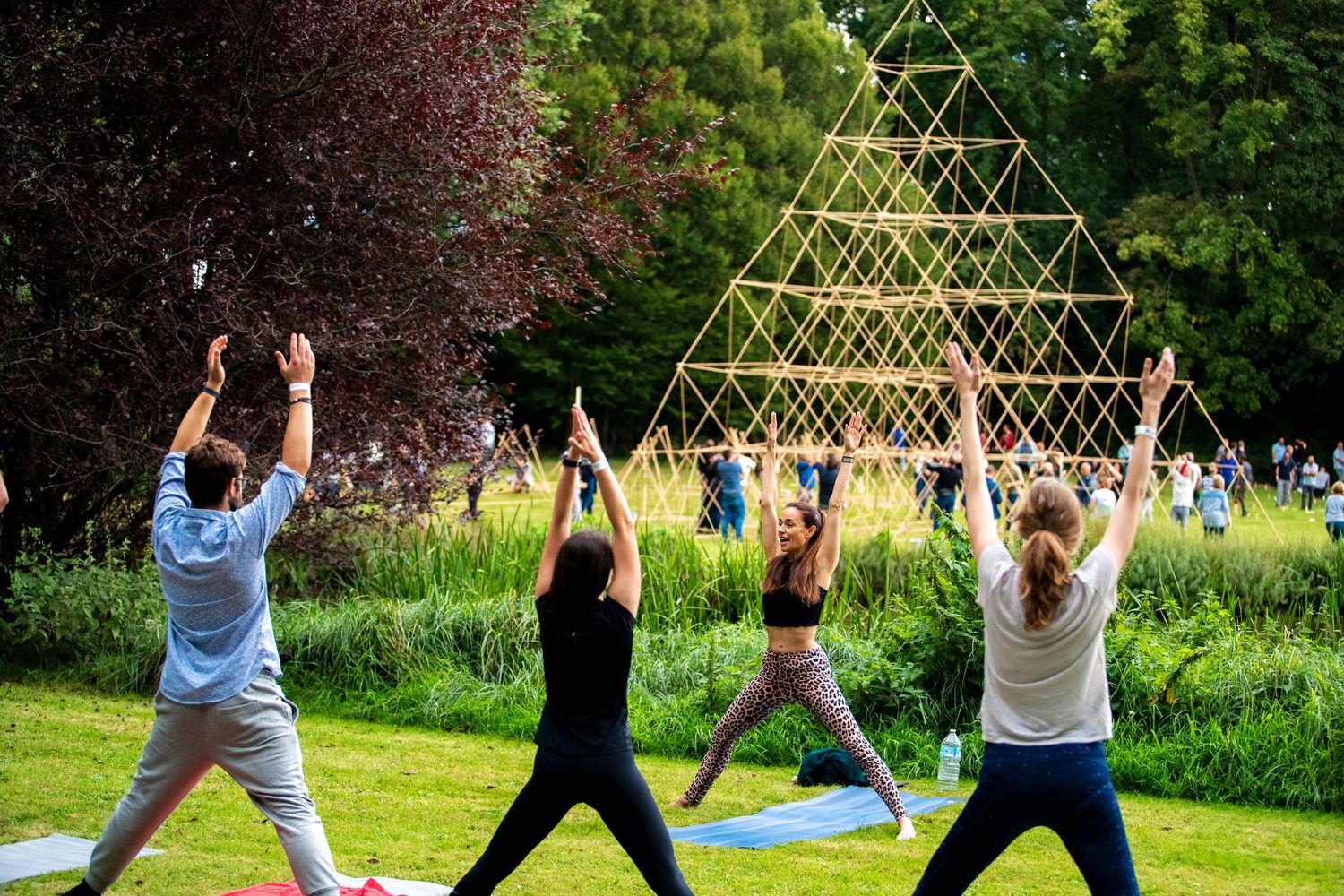 People practicing yoga outdoors with a geometric bamboo structure in the background.