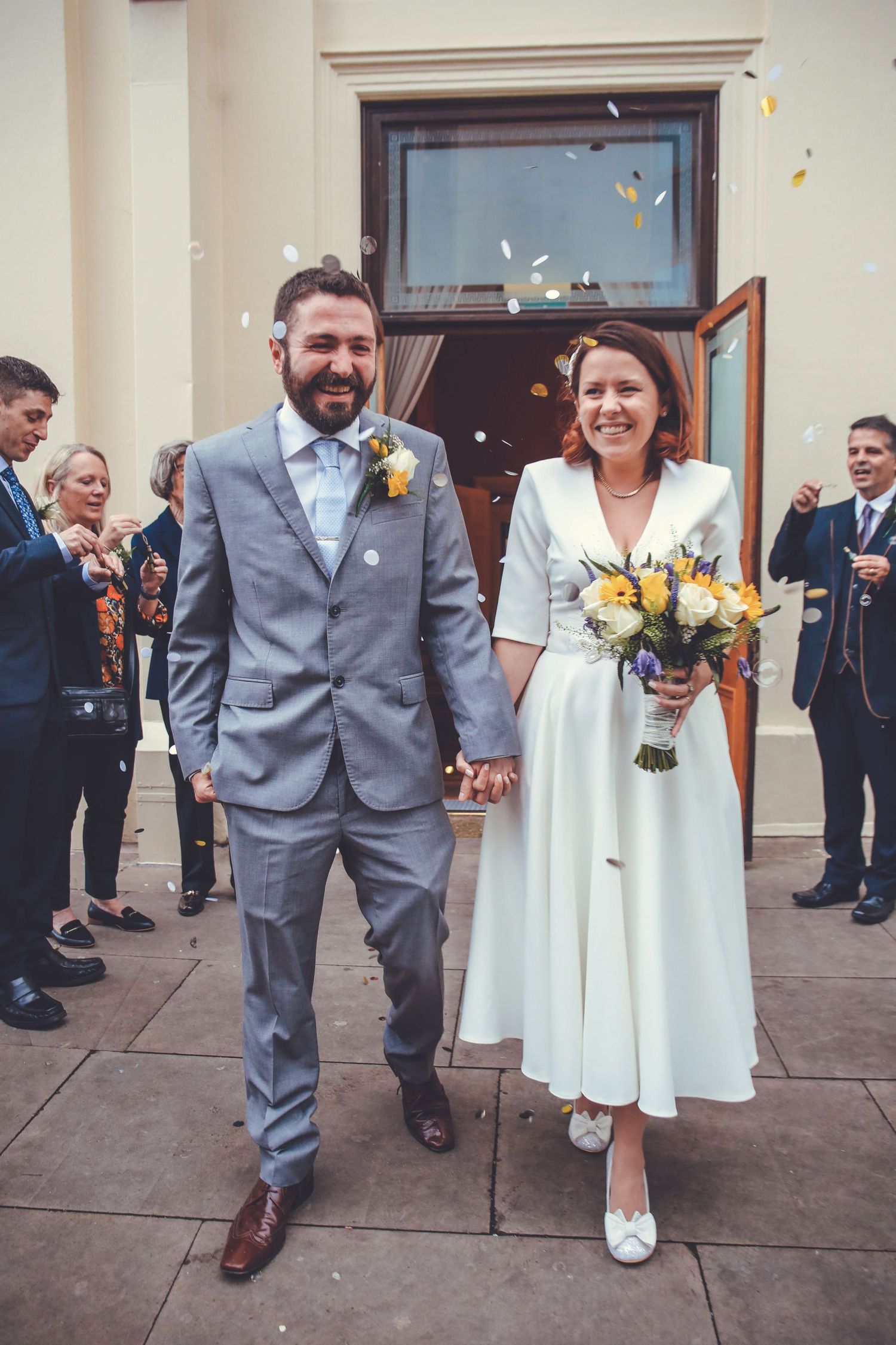 East Sussex wedding couple walking out of a Brighton wedding venue whilst confetti gets thrown at them by guests.