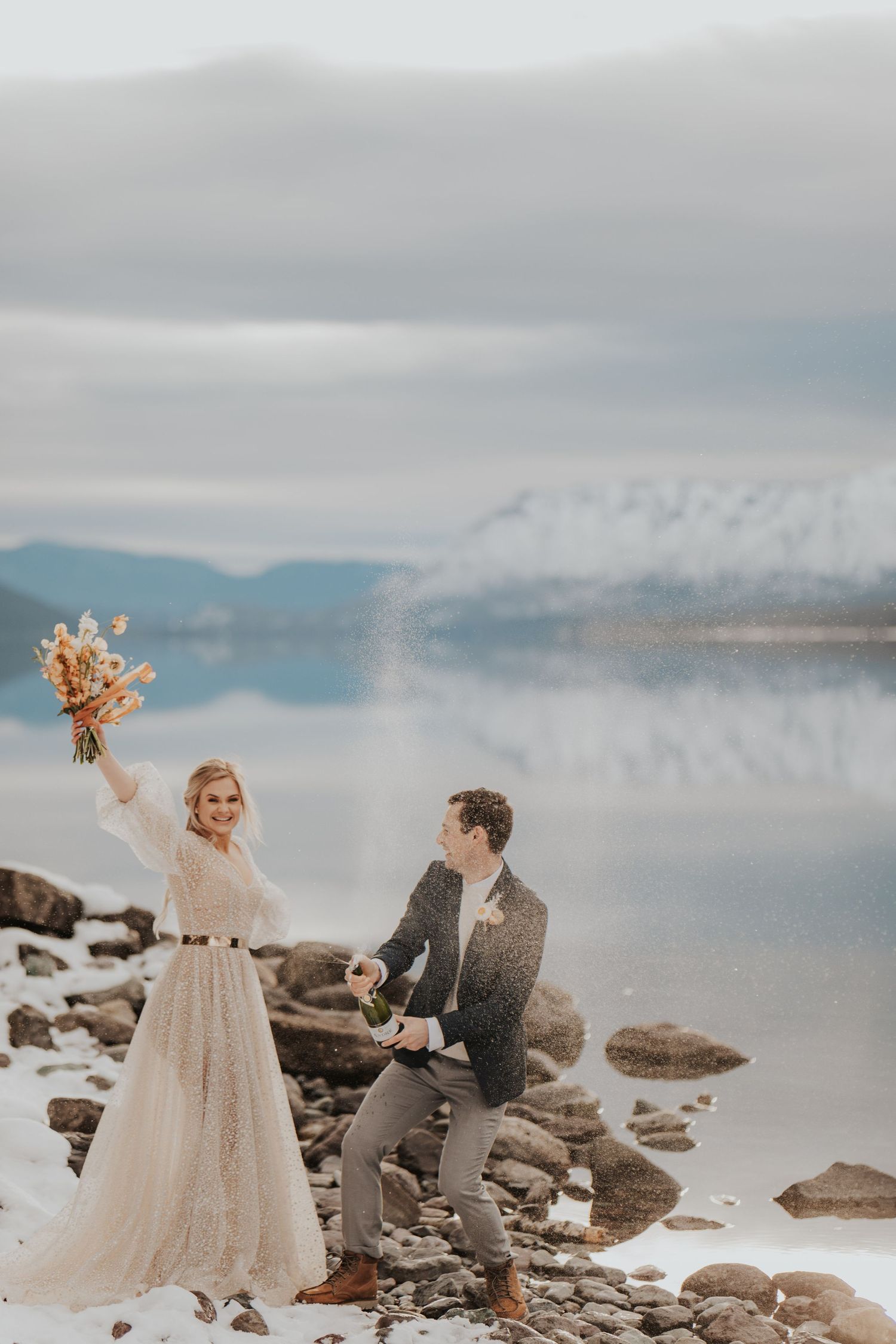 Eloping couple celebrate my popping a bottle of bubbly and laughing with one another