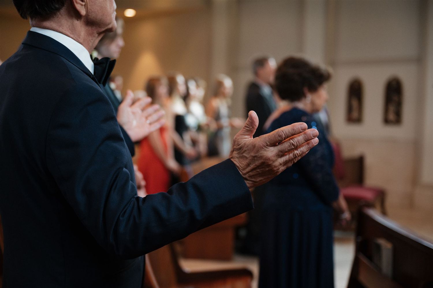 A person claps during a church ceremony while standing in formal attire.