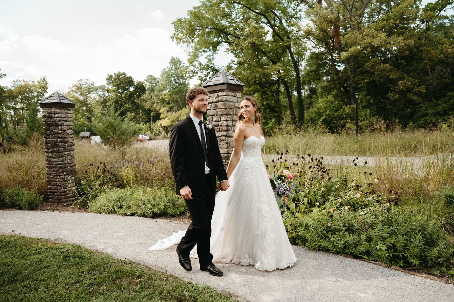 A couple walks along a garden path surrounded by blooming flowers.