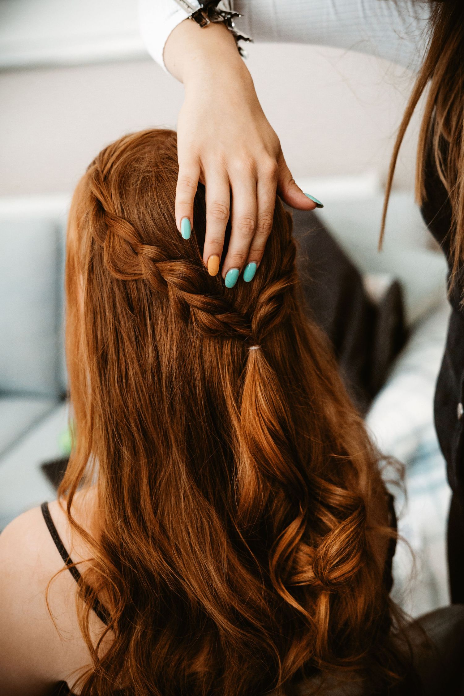 Hands with mint green nail polish braiding long auburn hair with soft waves and curls.