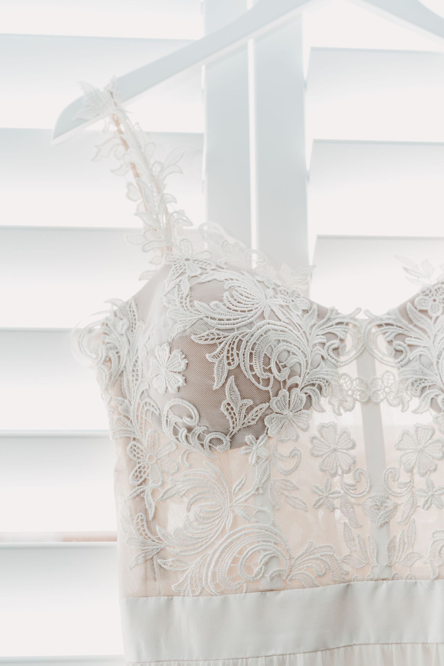 Close-up detail of delicate lace bodice on white wedding dress against venetian blinds.