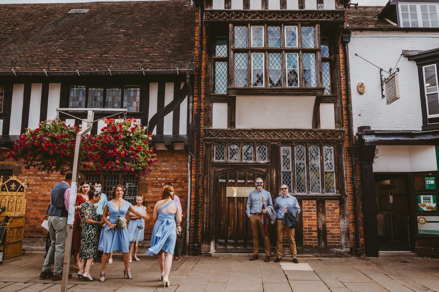Historic Tudor-style building facade with timber framing and hanging flower baskets.