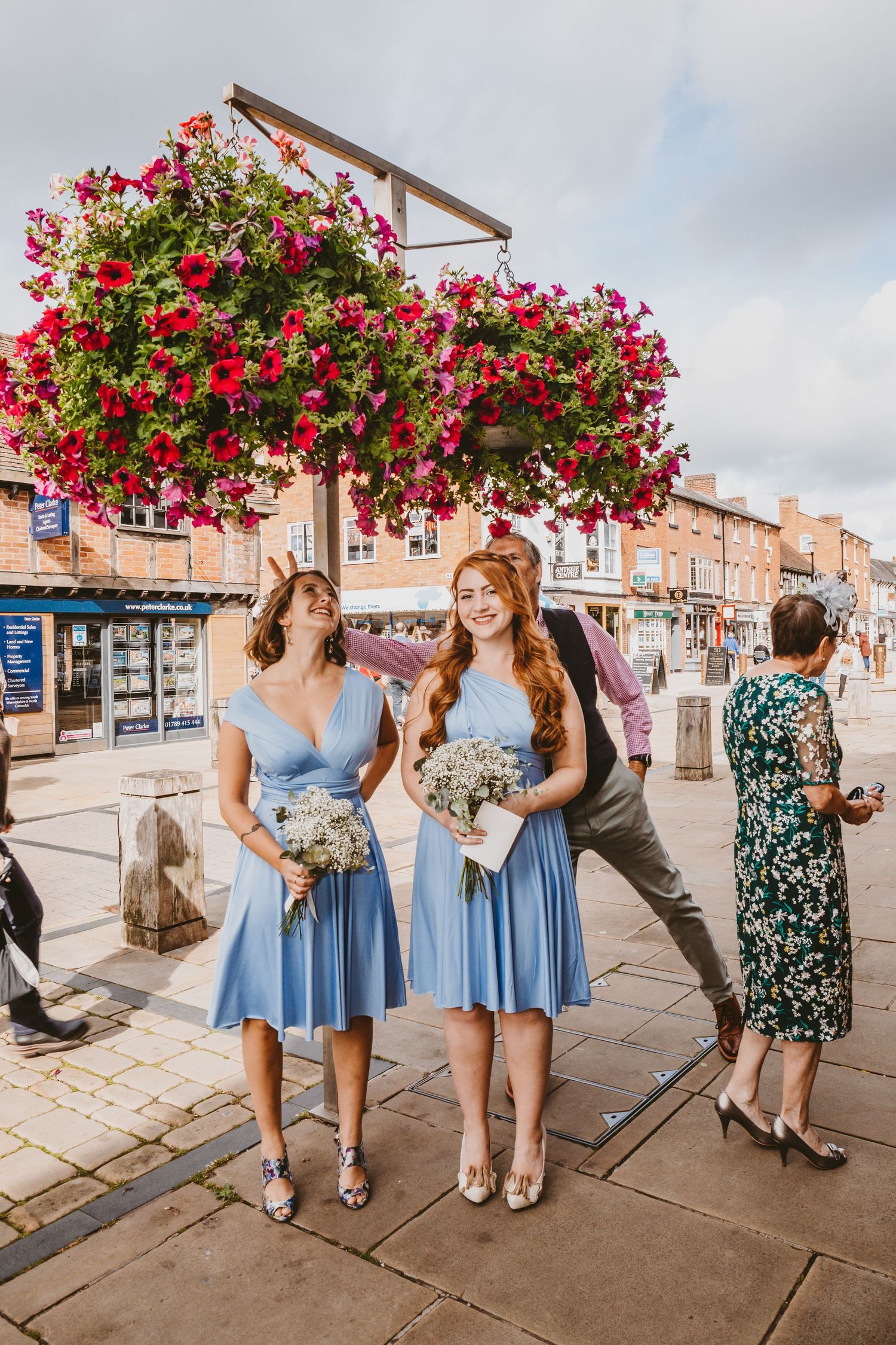 Street scene with vibrant hanging flower baskets and blue-dressed attendants holding bouquets.