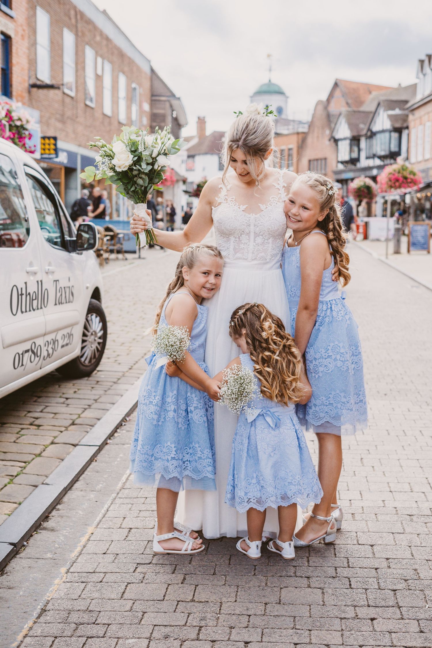 Wedding party on cobblestone street with light blue dresses and white floral bouquets.