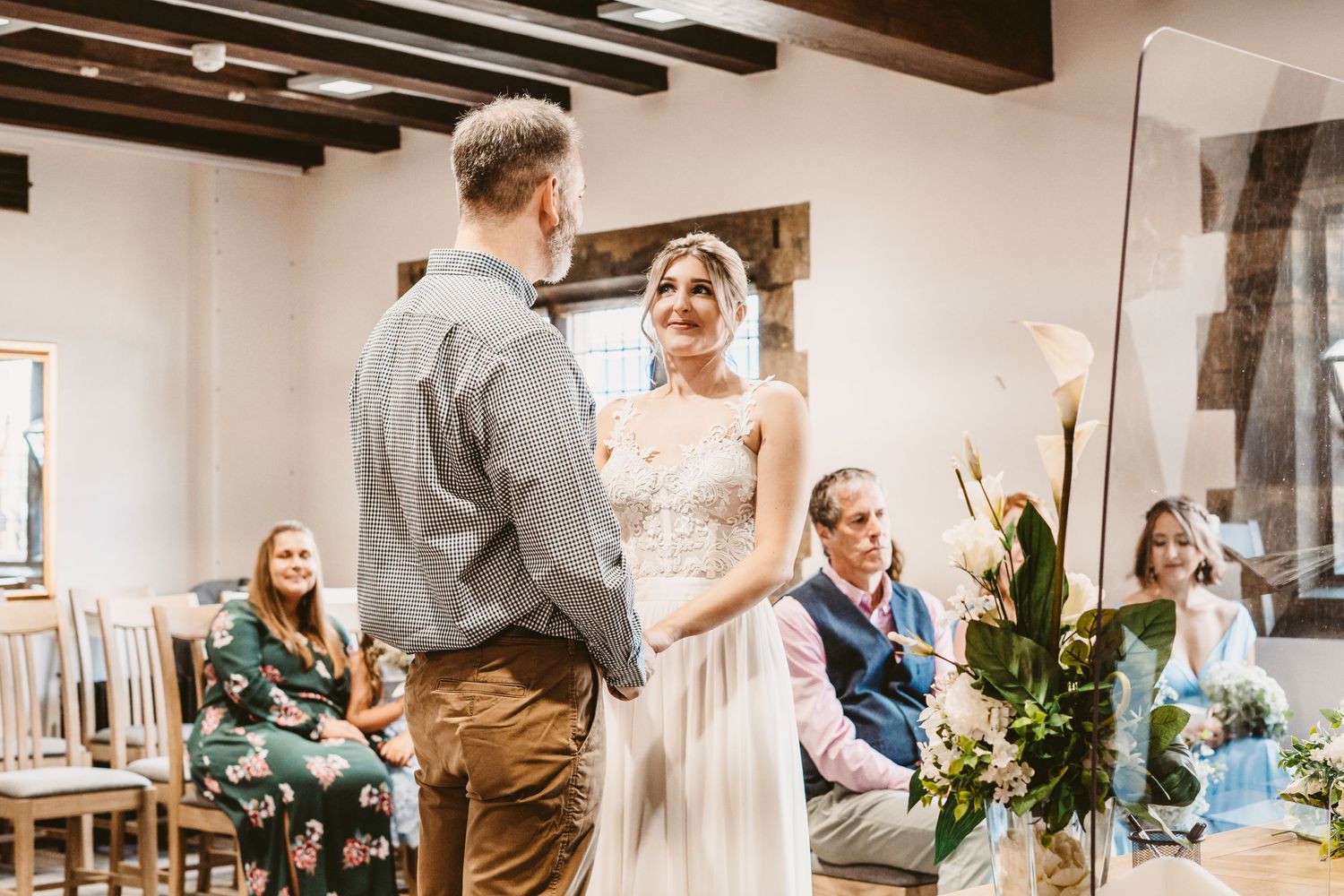 Intimate wedding ceremony in a rustic venue with wooden beams and greenery decorations.