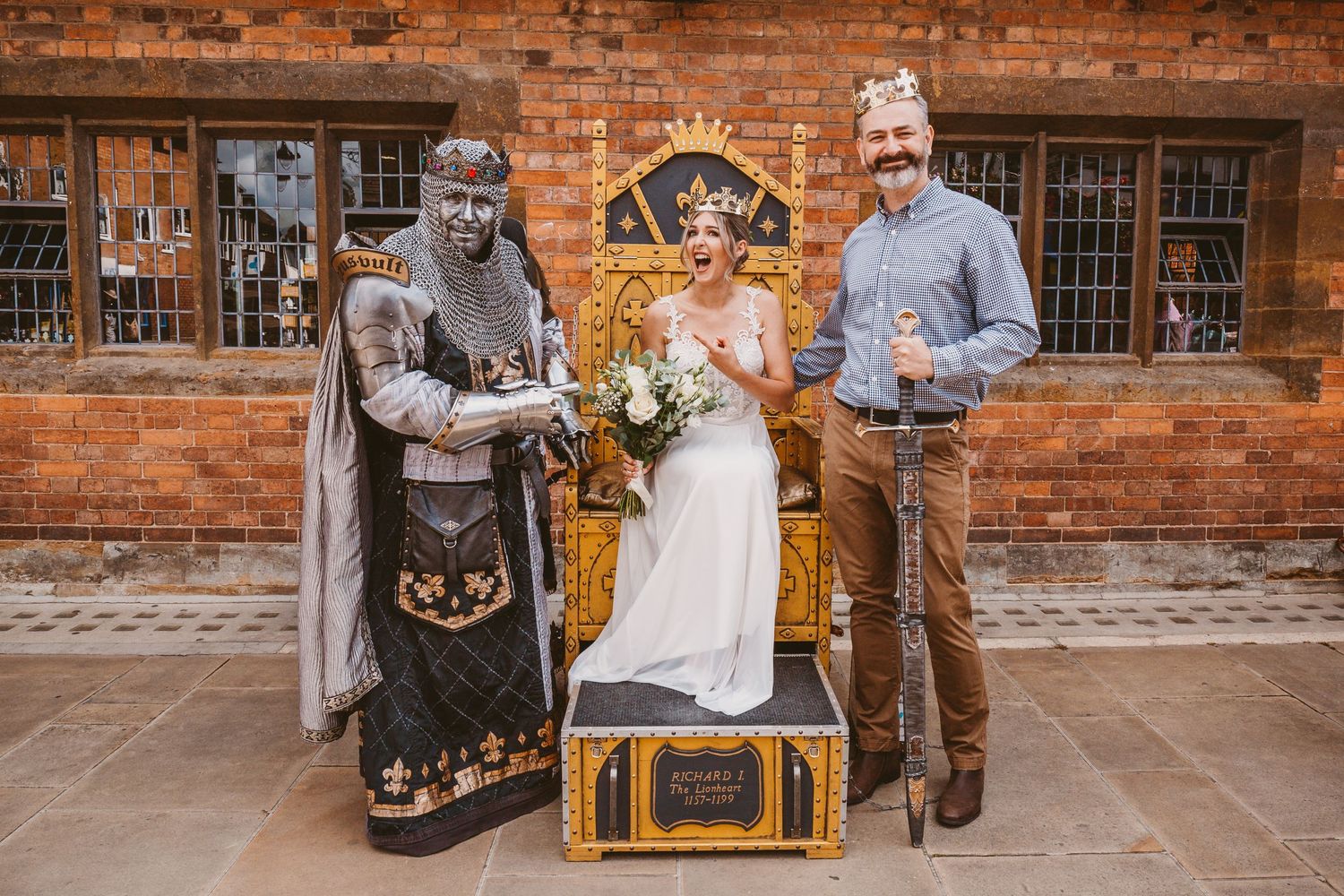 Wedding group posing with medieval knight statue and decorative throne.